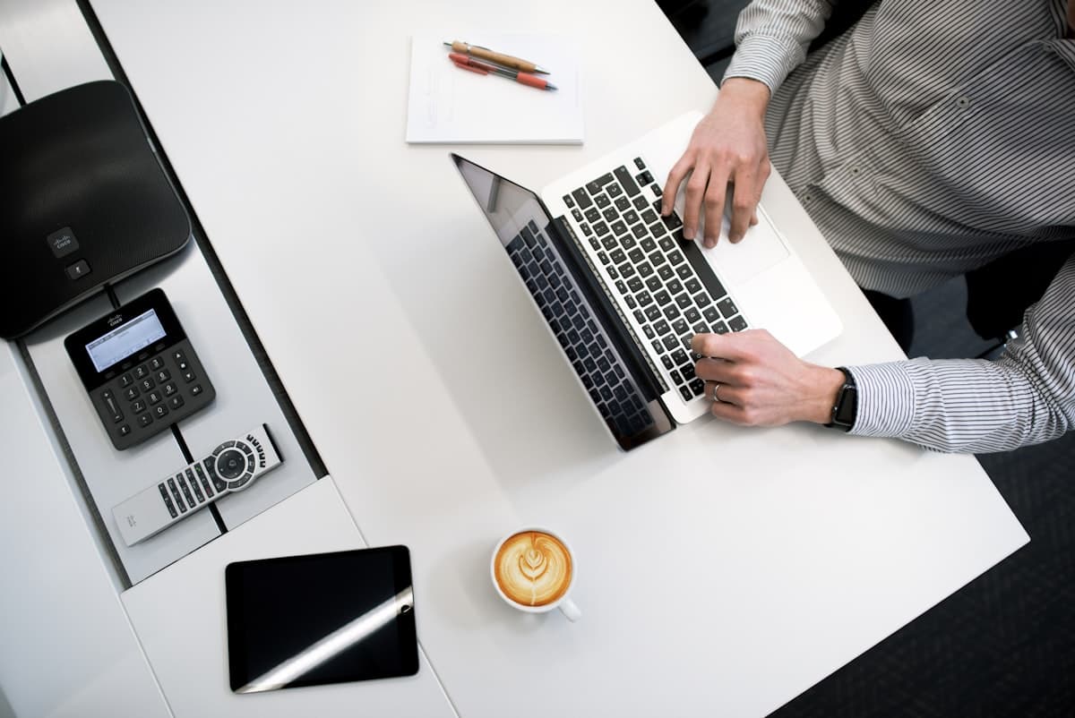 Overhead view of hands typing on a laptop, with a tablet and coffee nearby